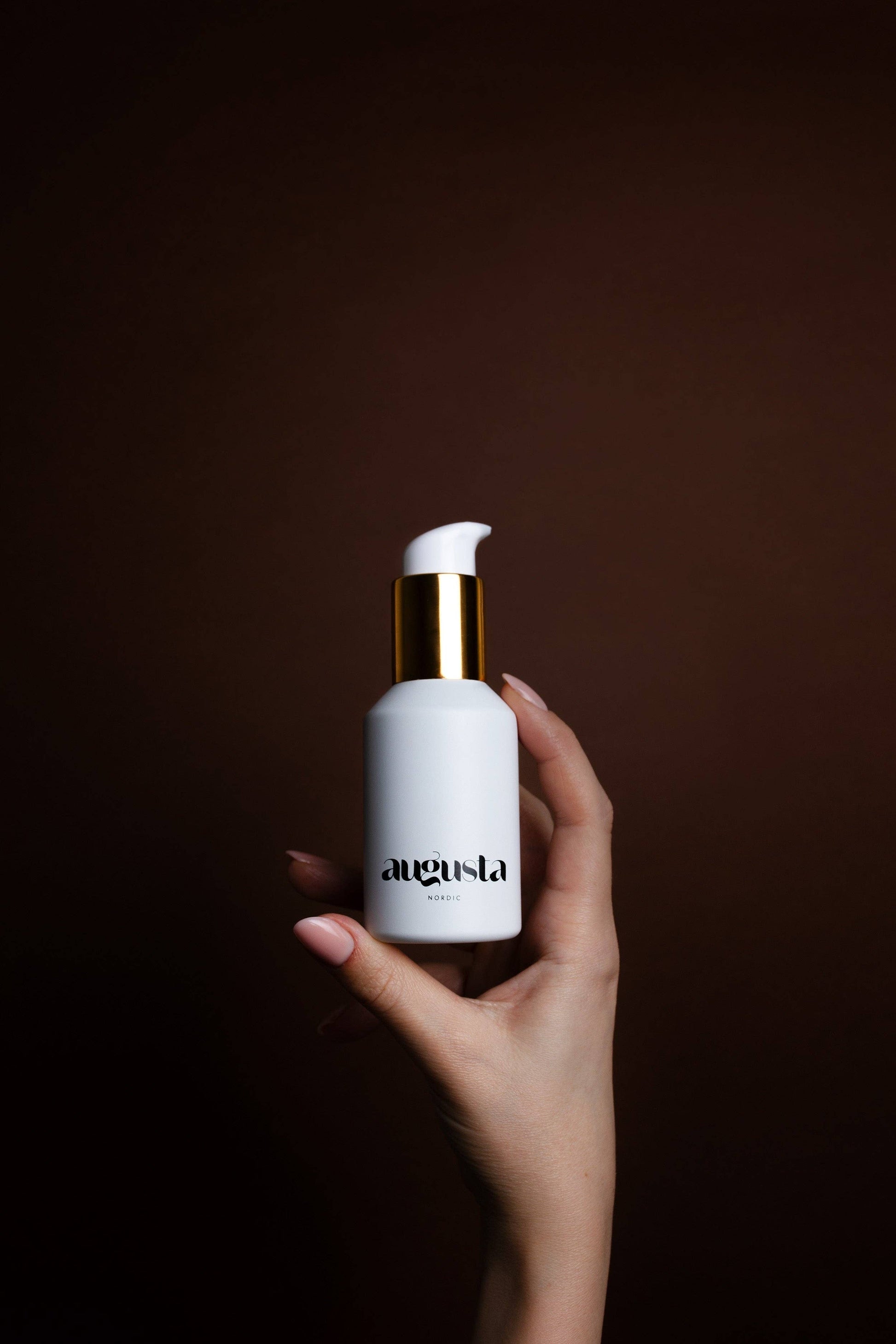 Hand holding a Augusta Nordic Soothing Hydration Gel white bottle with gold cap 